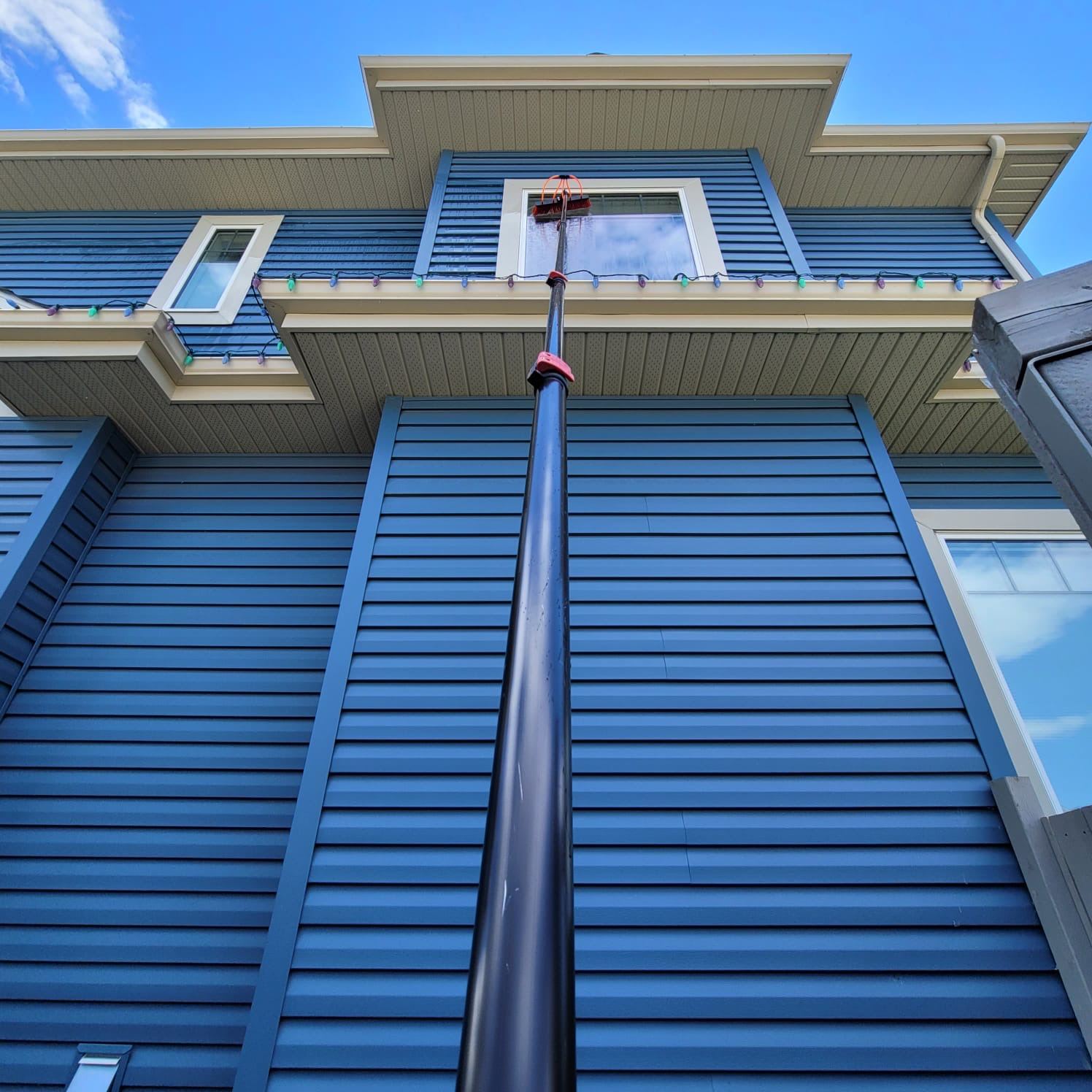 Delta Exterior technician using a water-fed pole to wash windows on a two-story home